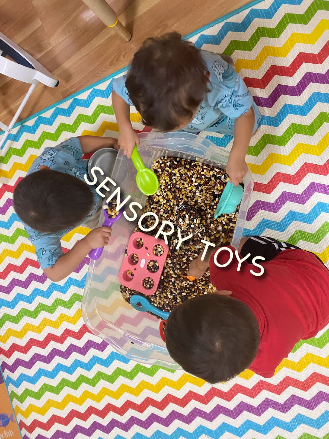 3 Kids playing with beach toys (shovel, cups, etc) in a bin full of dry beans of different sizes. 