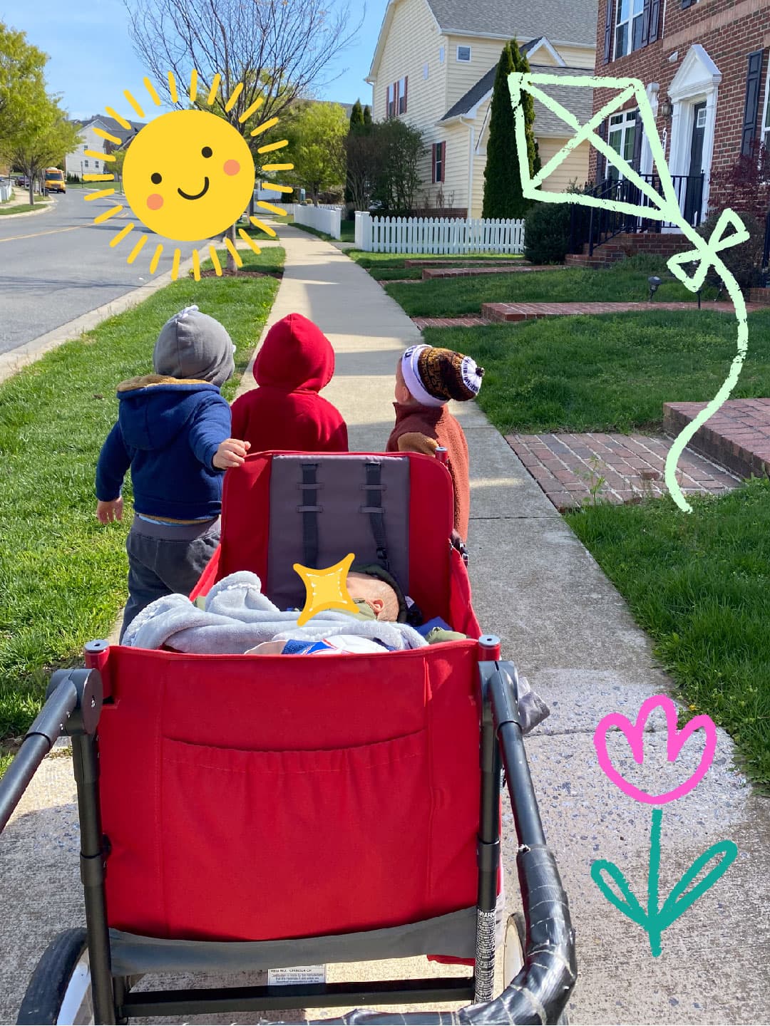 3 toddlers helping wheel an infant to the park with Ms Tina taking the photo. T